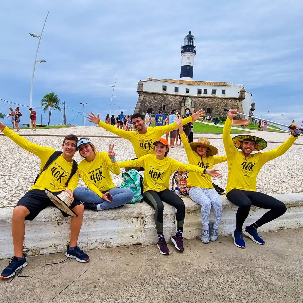 Participantes da 2ª edição, de camisa amarela, comemorando em frente ao Farol da Barra