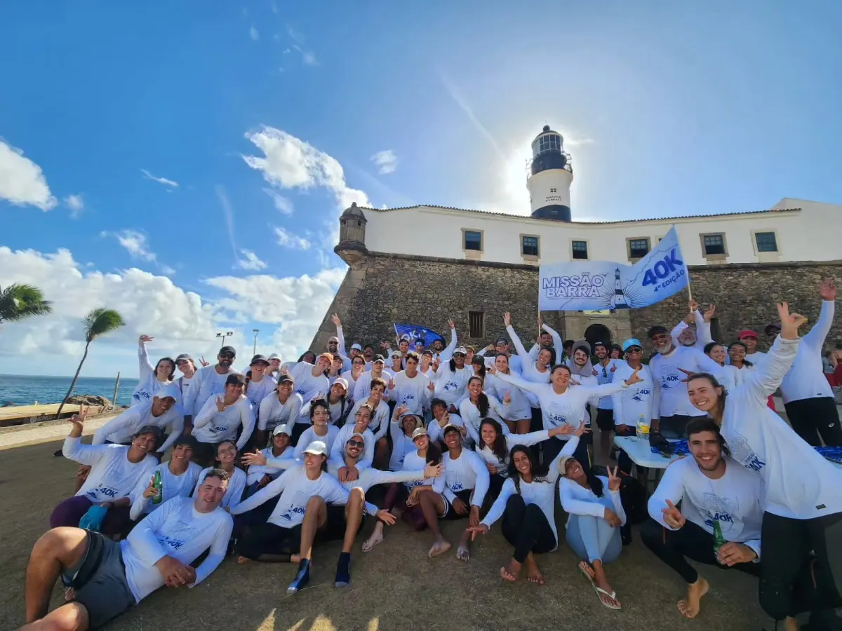 Participantes da 4ª edição, de camisa branca, reunidos com bandeiras em frente ao Farol da Barra