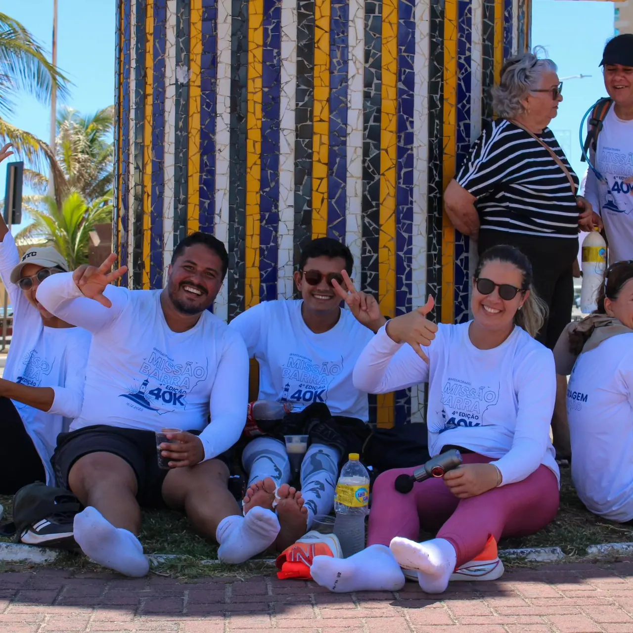 Participantes da 4ª edição sentados no chão durante uma parada, sorrindo para a câmera