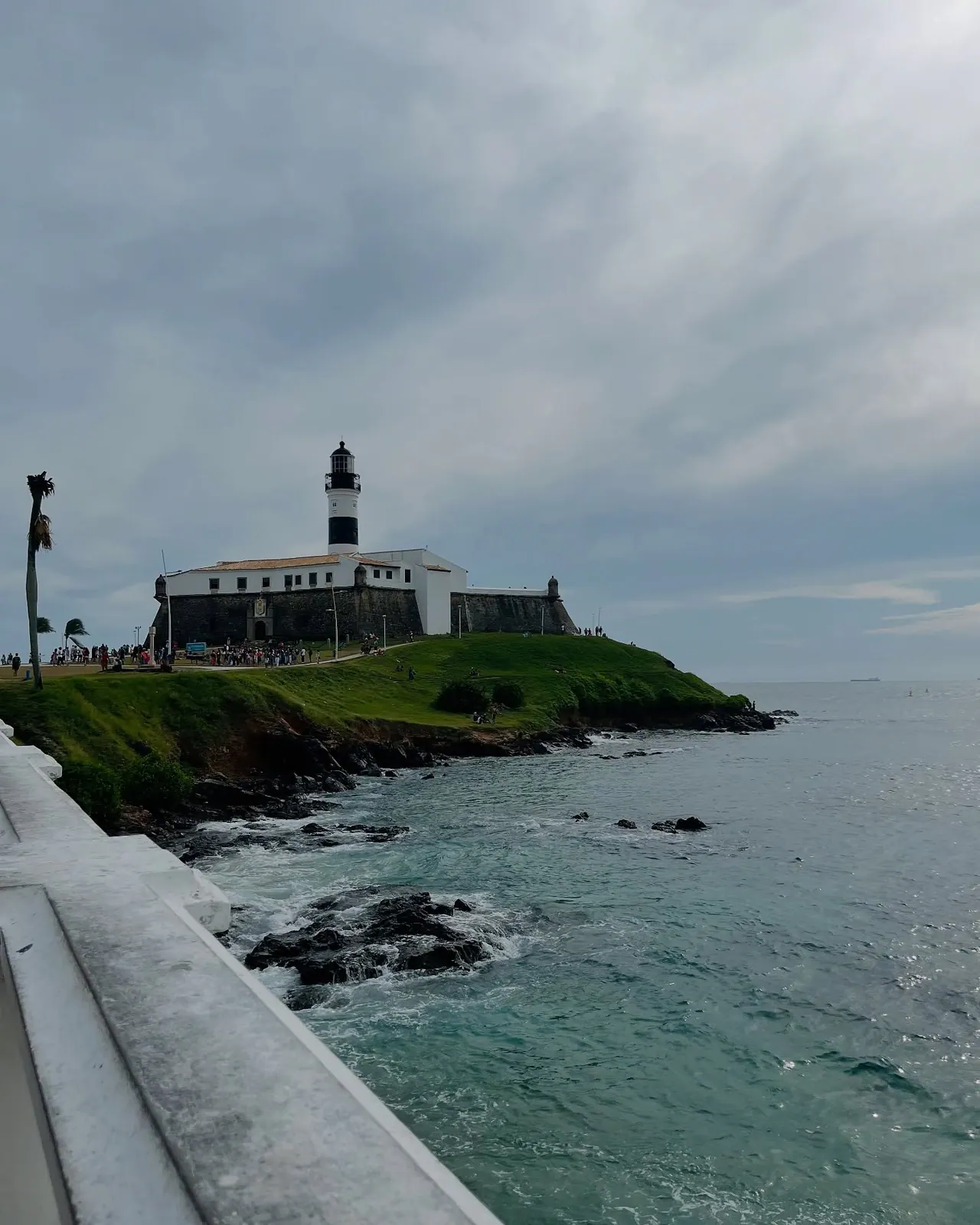 O Farol da Barra visto da orla, com o mar e as pedras em primeiro plano